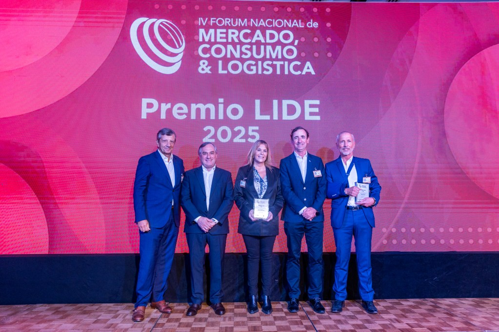 Entrega de premios en el IV Fórum Nacional de Mercado, Consumo & Logística, donde cuatro personas sostienen premios frente a un fondo con el logo del evento.