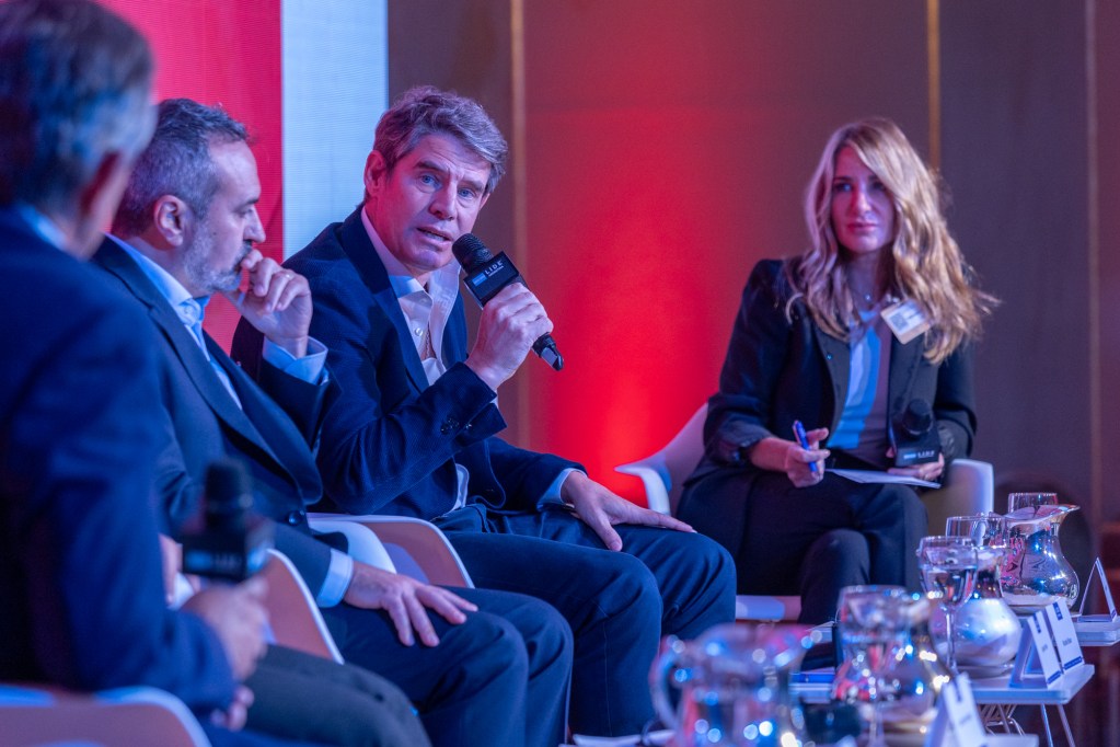 Panel de discusión en el IV Fórum Nacional de Mercado, Consumo & Logística, con varios oradores en un escenario iluminado.