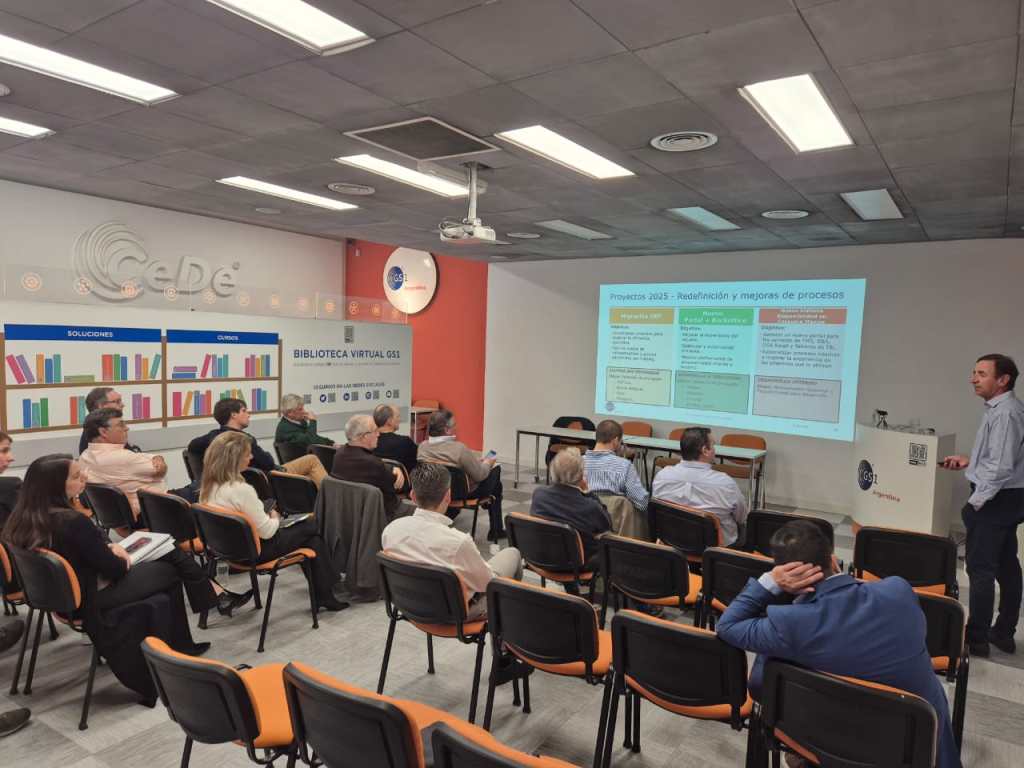 Reunión de la Asamblea General de GS1 Argentina con presentador frente a la audiencia, mostrando un proyector con proyectos y mejoras para el año 2025.