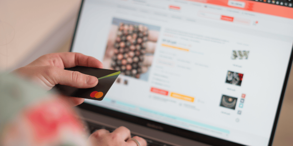 A person holding a credit card in front of a laptop displaying an online shopping website.