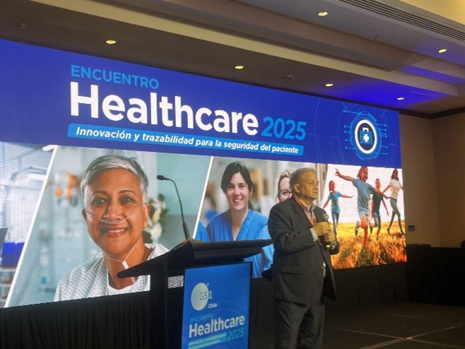 Un orador en el Encuentro Healthcare 2025, con una presentación detrás que muestra imágenes de atención médica y un enfoque en la innovación y la seguridad del paciente.