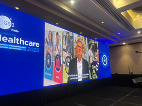 Un orador en un escenario durante el Encuentro Healthcare 2025, con pantallas que exhiben logos y contenido relacionado con el evento.